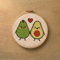Embroidery hoop with punch needled two smiling avocados and a heart on a wooden surface