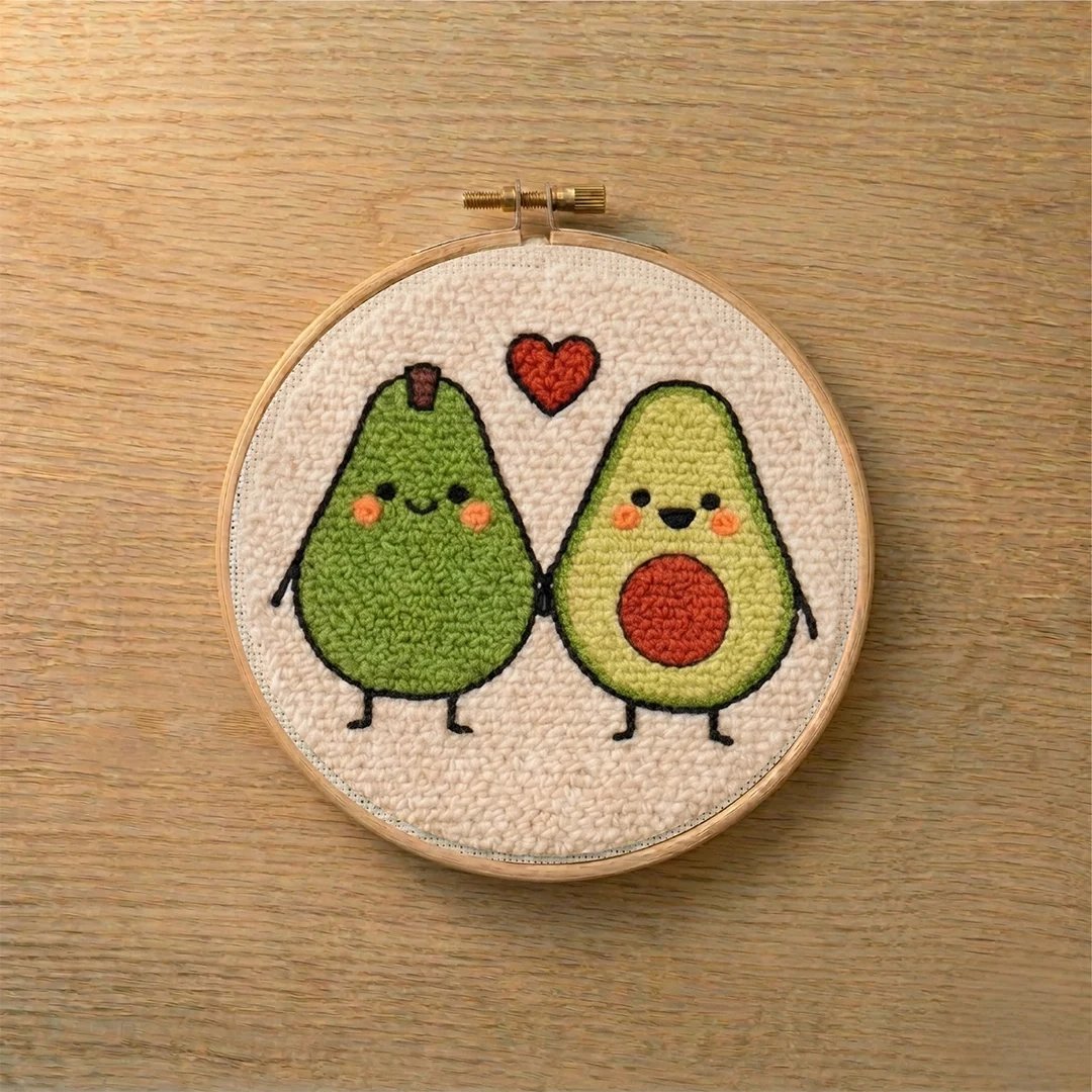 Embroidery hoop with punch needled two smiling avocados and a heart on a wooden surface