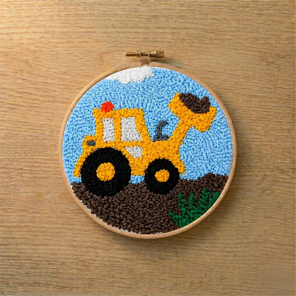 Embroidery hoop with a punch needled yellow bulldozer design on a wooden surface