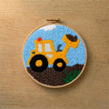 Embroidery hoop with a punch needled yellow bulldozer design on a wooden surface