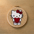 Embroidery hoop with a punch needled kitty character holding a heart on a wooden surface