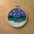 Embroidery hoop with punch needled night sky scene on a wooden surface