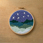 Embroidery hoop with punch needled night sky scene on a wooden surface