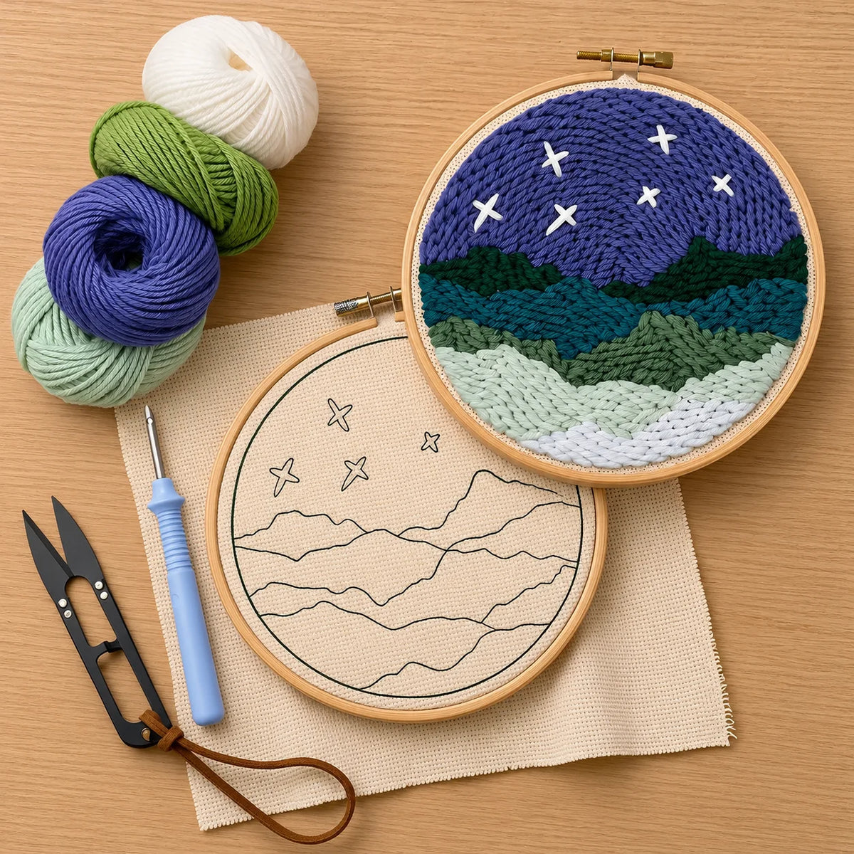 Embroidery hoops with punch needled landscape designs on a wooden surface with yarn and tools.