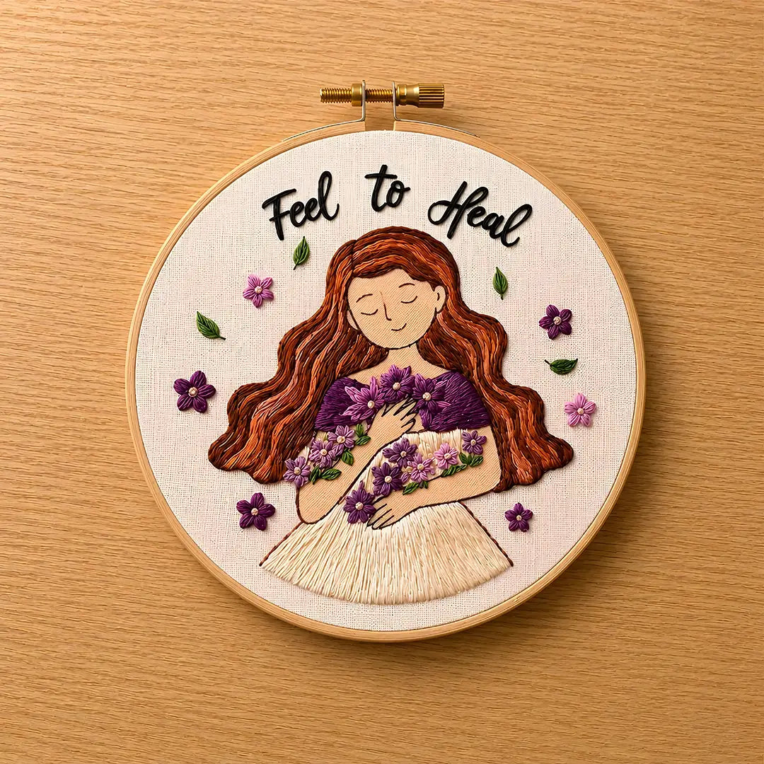 Embroidery hoop with a woman holding flowers and 'Feel to Heal' text on a wooden background