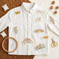 White shirt with floral stitch and stitch stickers with embroidery tools on textured surface