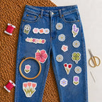 Blue jeans with flower-themed stitch and stitch stickers on blue jean on textured surface with embroidery tools like hoop, needle, threads and scissors 