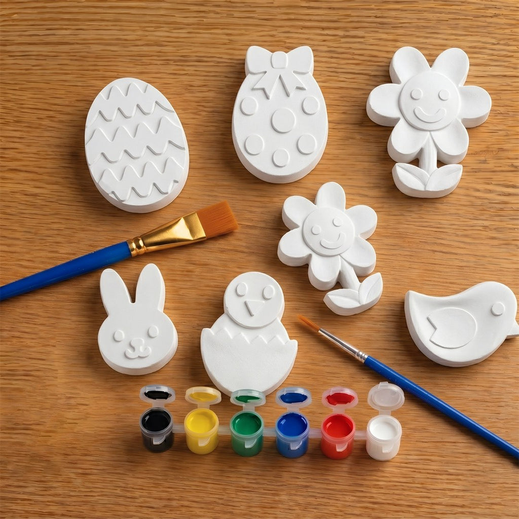 Set of white concrete  molds shaped like animals on a wooden surface with paintbrushes and paint.