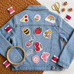 Garden-themed stitch and stitch stickers on blue jacket on textured surface with embroidery tools like hoop, needle, threads and scissors 