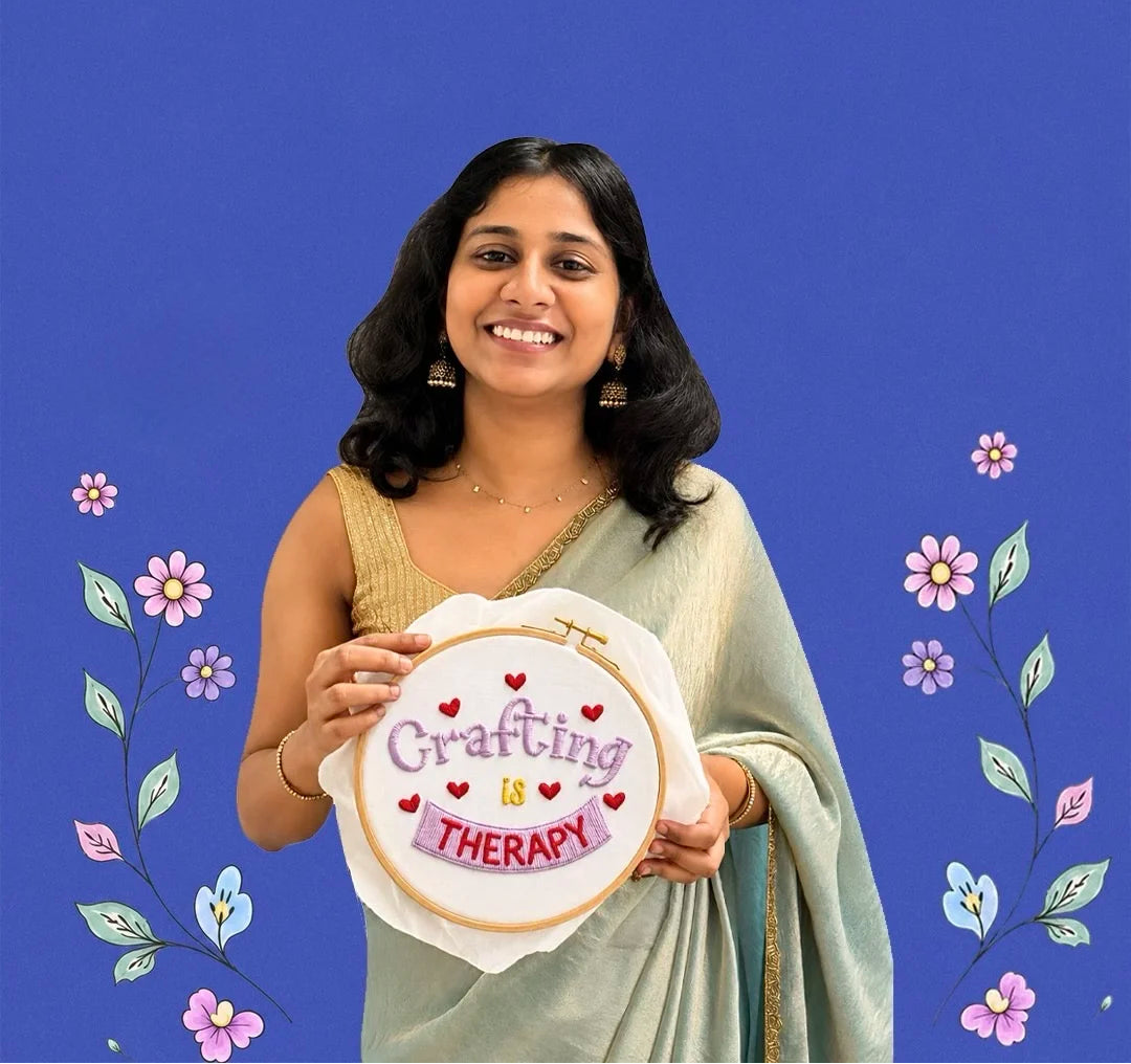Woman holding a embroidery hoop with 'Crafting is Therapy' text against a blue background with floral decorations.