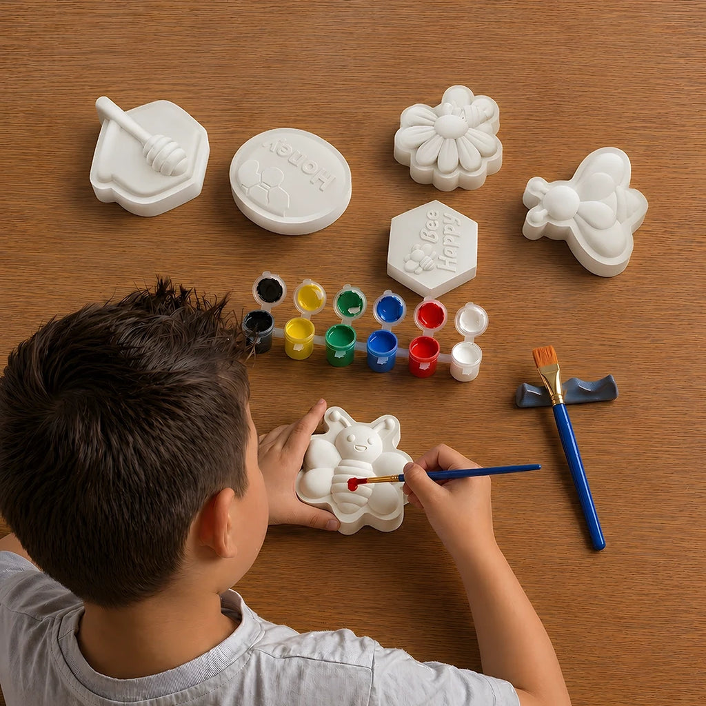 Child painting a white concrete mold shapes with various other shapes and paint supplies on a wooden table.