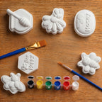 White concrete  honeycomb molds with bee designs on a wooden surface, accompanied by paintbrushes and paint.