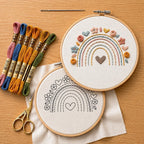 Embroidery hoops with rainbow and heart designs, colorful threads, and scissors on a wooden surface.