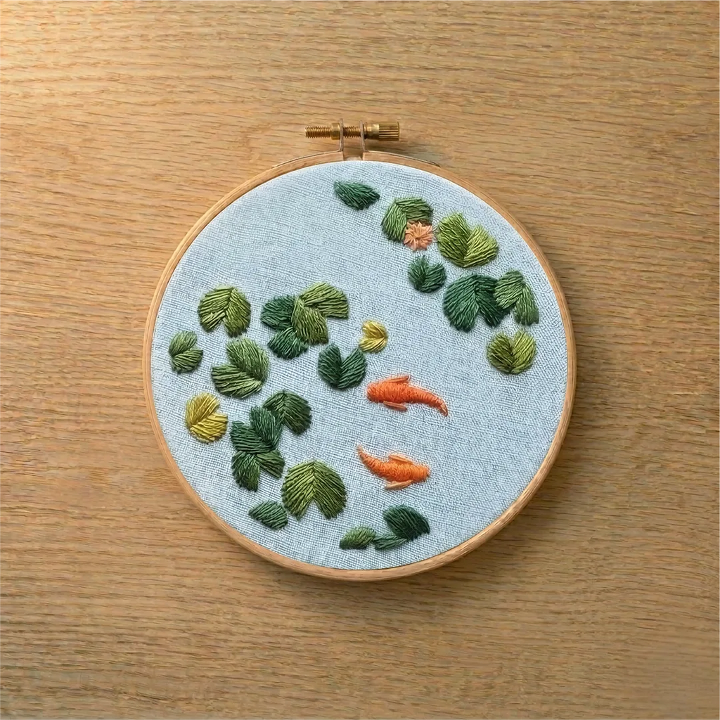 Embroidery hoop with embroidered fish and plants on a wooden surface