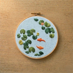 Embroidery hoop with embroidered fish and plants on a wooden surface