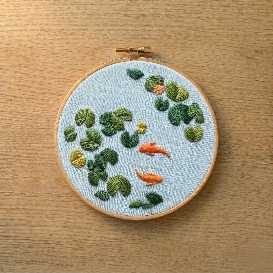 Embroidery hoop with embroidered fish and plants on a wooden surface