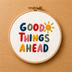 Embroidery hoop with 'Good Things Ahead' text and sun design on a wooden surface