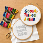 Embroidery hoops with 'Good Things Ahead' text and colorful threads on a wooden surface.