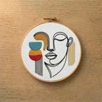 Embroidery hoop with abstract face design on a wooden surface