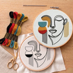 Embroidery hoops with face designs and colorful thread on a wooden surface