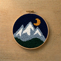 Embroidery hoop with mountain and moon design on a wooden surface