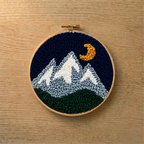 Embroidery hoop with mountain and moon design on a wooden surface