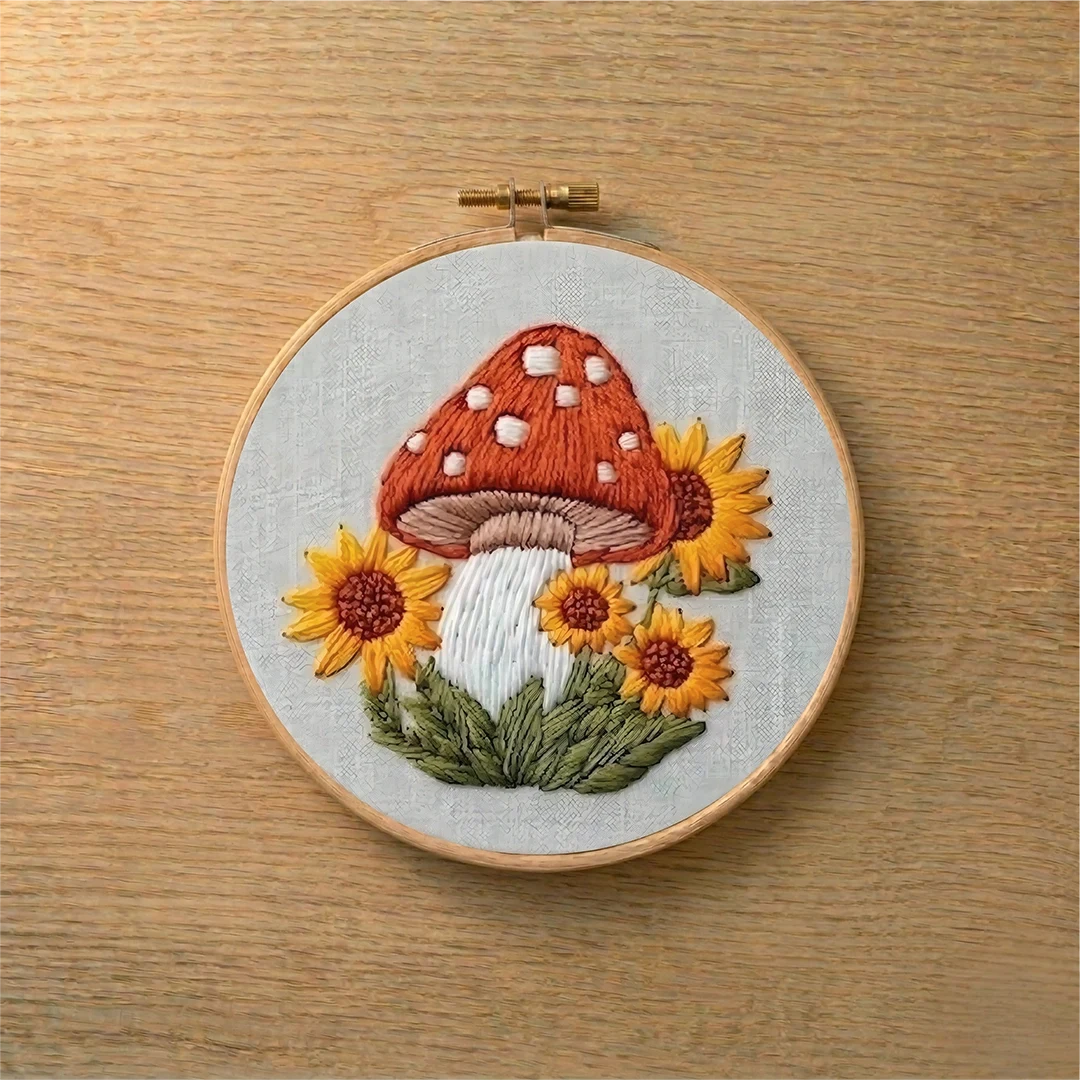 Embroidery hoop with a mushroom and sunflower design on a wooden surface