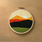 Embroidery hoop with a punch needled landscape design on a wooden surface