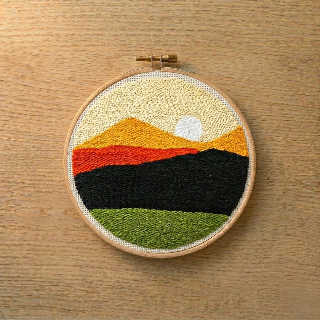 Embroidery hoop with a punch needled landscape design on a wooden surface