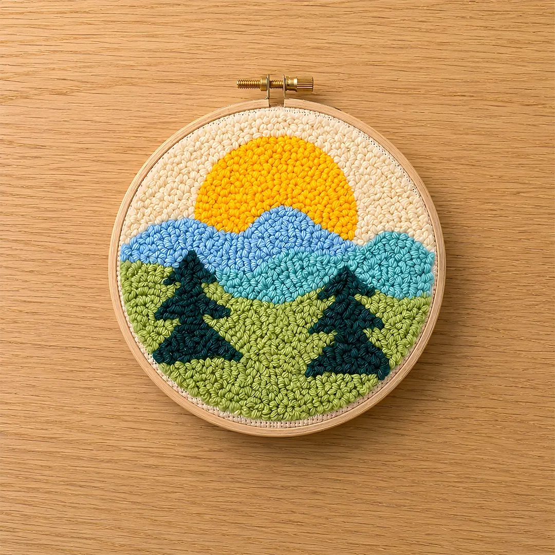 Embroidery hoop with a punch needled landscape design featuring trees, mountains, and a sun on a wooden surface.