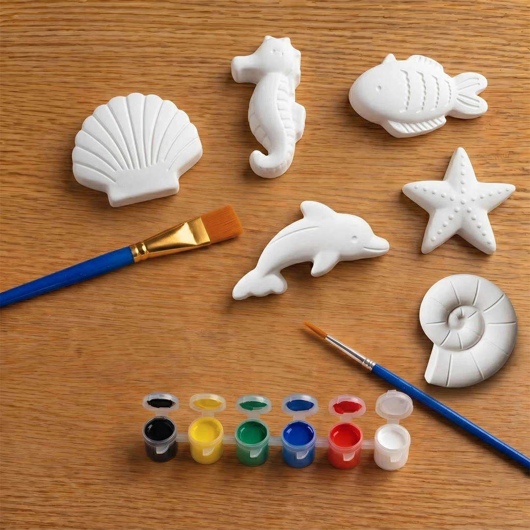 Set of white concrete  sea creature molds on a wooden surface with paintbrushes and paint.