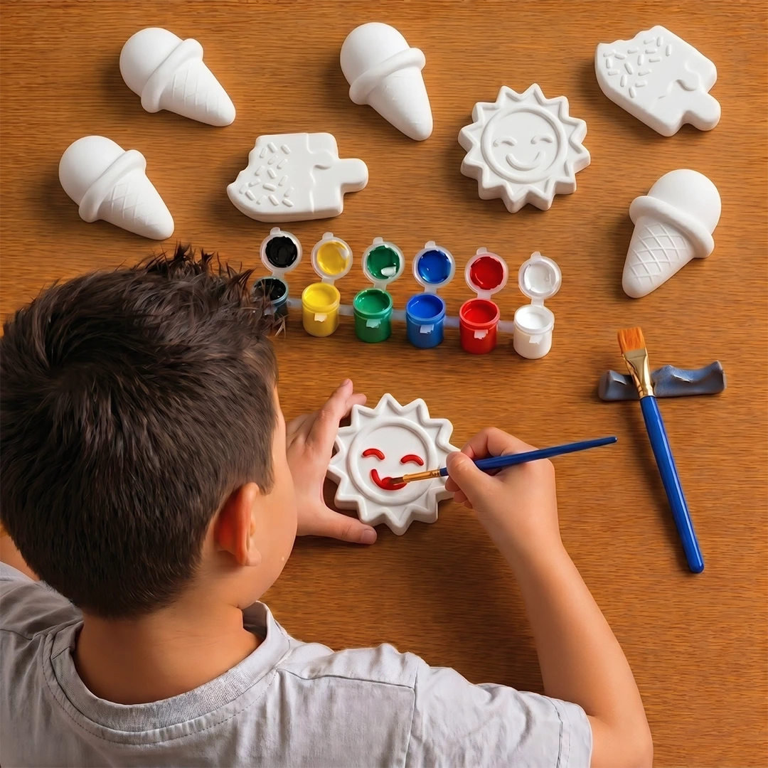 A boy painting sun shaped concrete toy with paint brush. other shapes such as ice cream cones, suns, and clouds on a wooden surface with paintbrushes and paint.