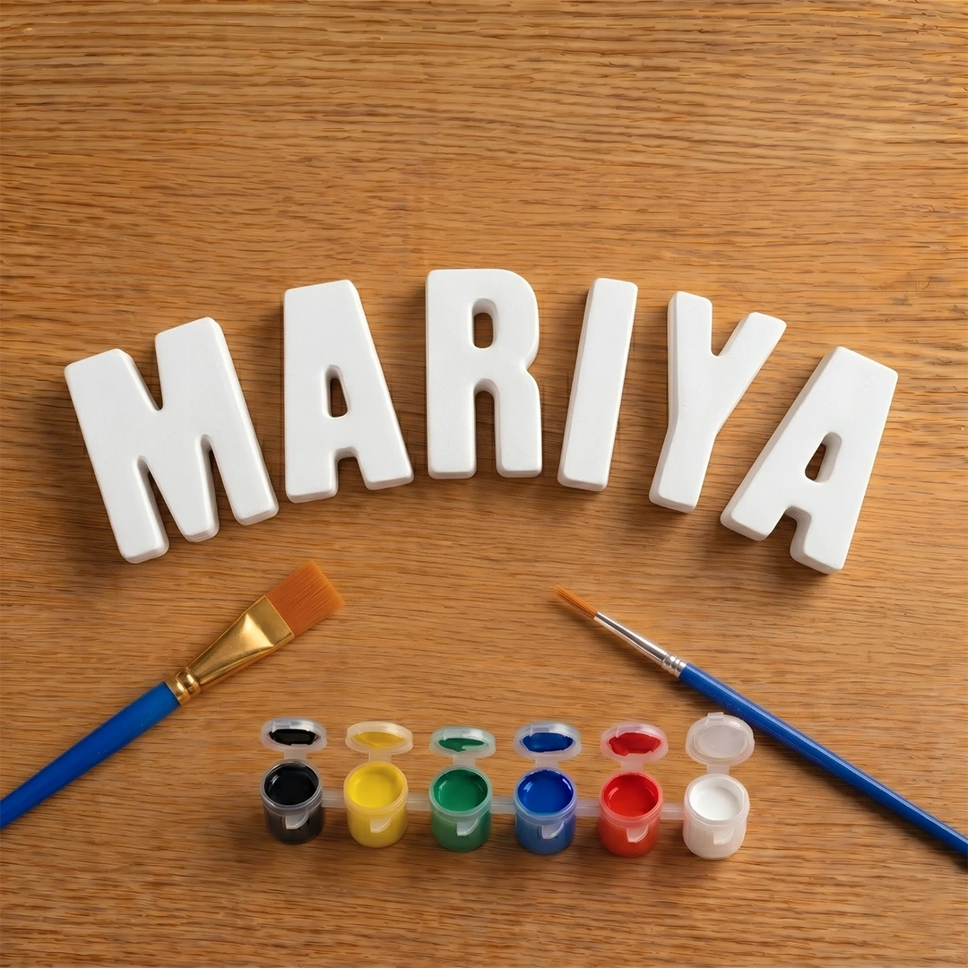 White letters spelling 'MARIYA' on a wooden surface with paintbrushes and paint containers.
