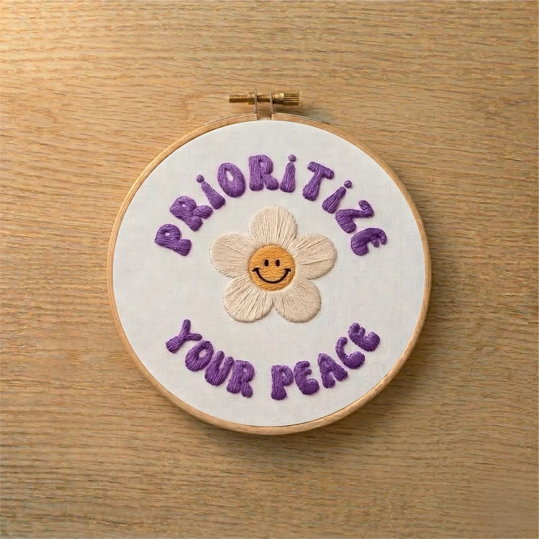 Embroidery hoop with 'Prioritize Your Peace' text and a smiley flower on a wooden surface