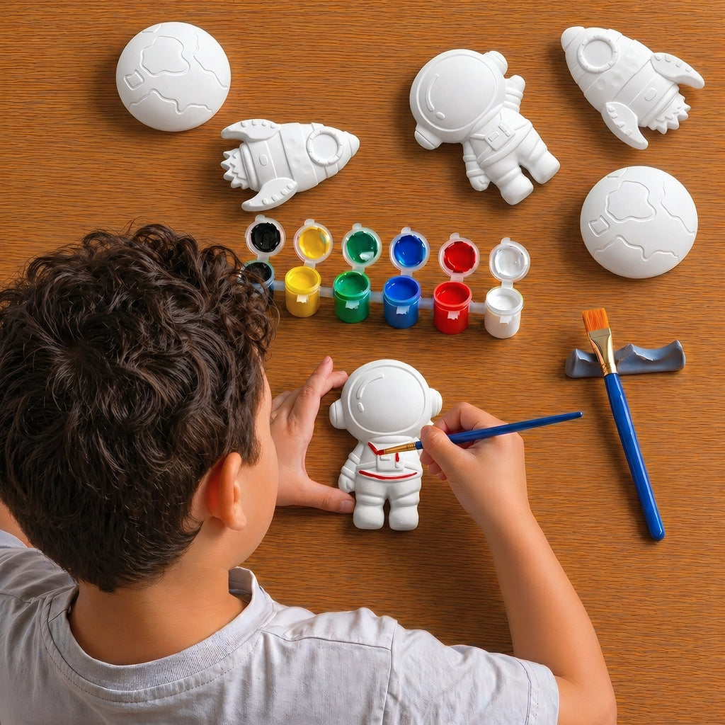 Child painting white concrete objects shaped like space-themed items on a wooden table.