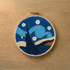 Embroidery hoop with a punch needled starry night design on a wooden surface