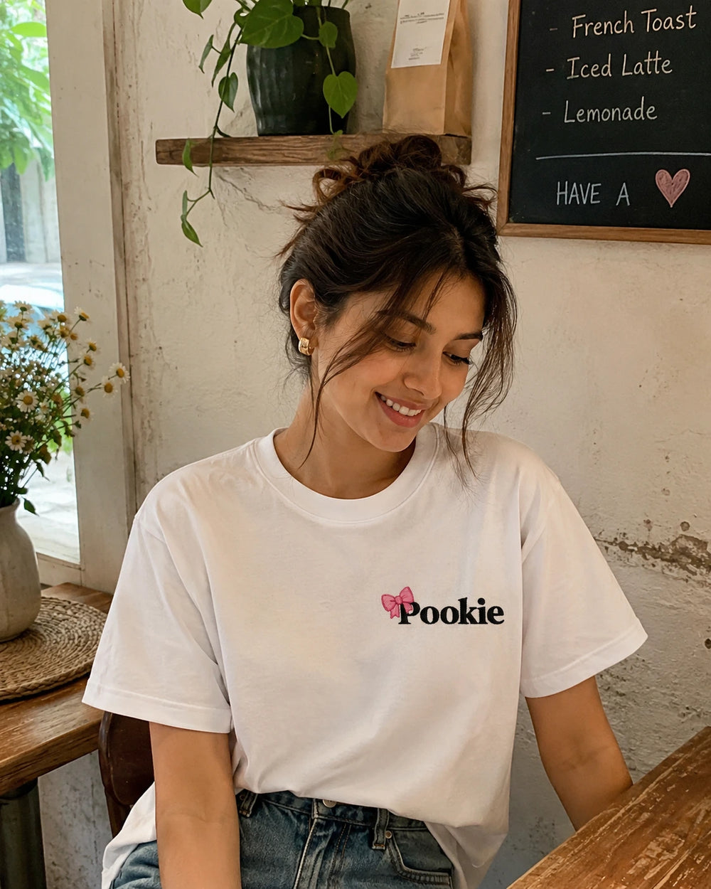 Woman wearing a white t-shirt with  'Pookie' design stitched using stick and stitch stickers in a cafe setting