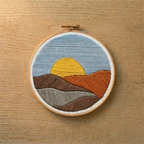 Embroidery hoop with a landscape design featuring a sunset on a wooden surface
