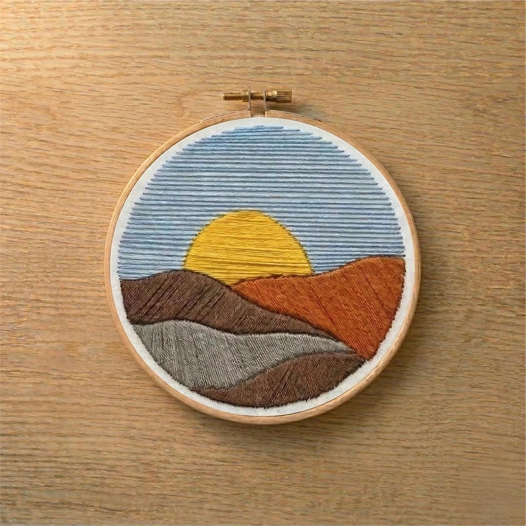Embroidery hoop with a landscape design featuring a sunset on a wooden surface