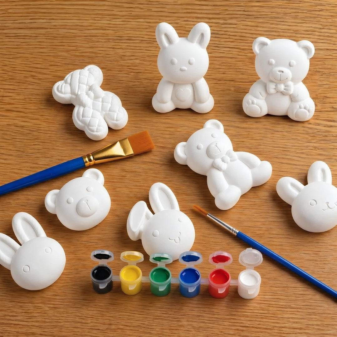 White concrete  animal figurines on a wooden surface with paintbrushes and paint cans.