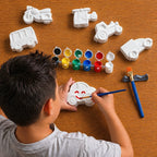 Child painting a toy car with various paint colors and tools on a wooden table.