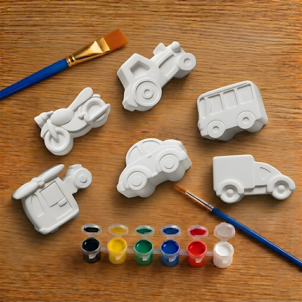 White concrete molds shaped like cars on a wooden surface with paintbrushes and paint.