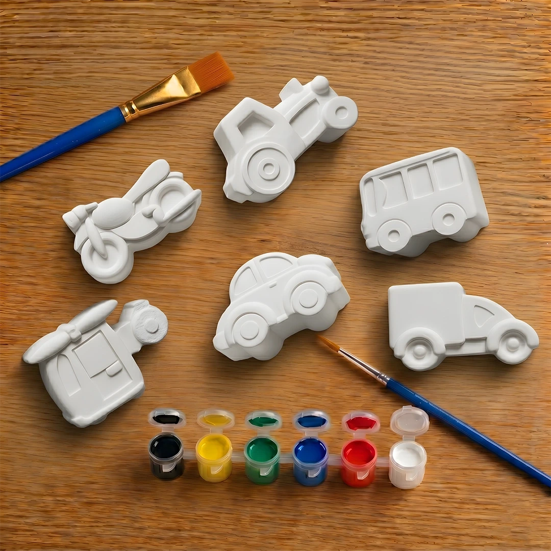 White concrete molds shaped like cars on a wooden surface with paintbrushes and paint.