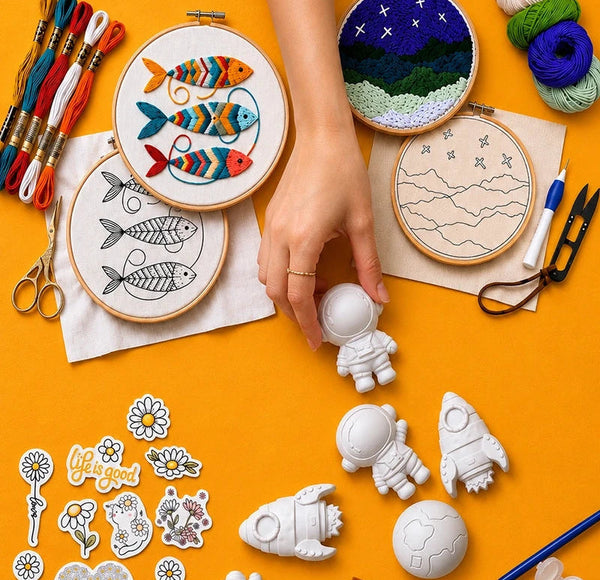 Embroidery hoops with colorful fish design on a yellow background, surrounded by concrete shapes and art supplies.